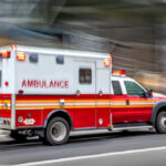 Red and white ambulance driving on a city street.