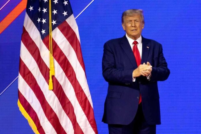 shutterstock_2272007717.jpg featured image Donald Trump in suit near the American flag on stage.