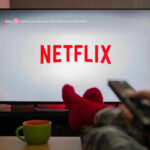 Person watching Netflix with remote and drink.