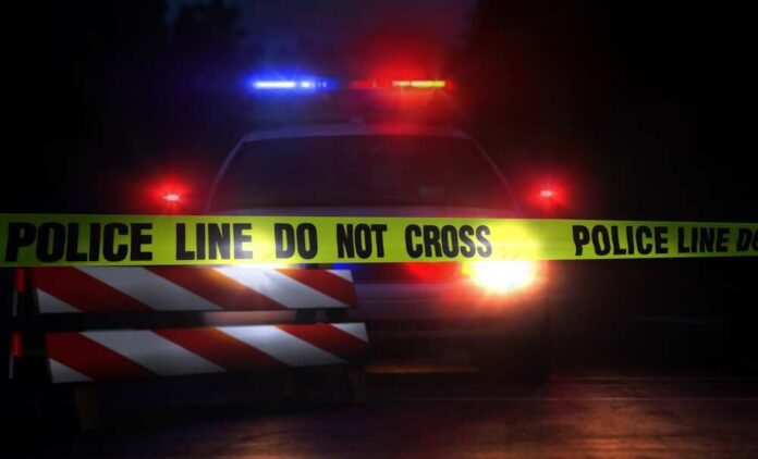 Police car with flashing lights behind caution tape.