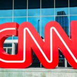 CNN Fires Top Reporter Red CNN logo outside a building entrance.