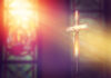 Crucifix with sunlight, stained glass window in background.