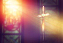 Crucifix with sunlight, stained glass window in background.