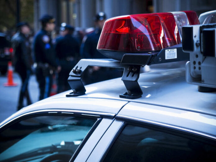 shutterstock_46269745.jpg featured image Police car roof with lights, officers in background.
