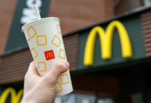Hand holding McDonald's cup in front of restaurant sign