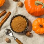 A bowl of pumpkin spice surrounded by pumpkins and cinnamon sticks