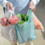 Person carrying grocery bags with vegetables and fruits.