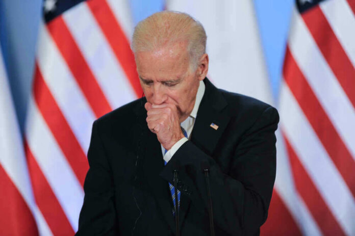 Joe Biden coughing in a suit standing in front of flags