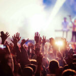 Concert crowd with hands raised, bright stage lights