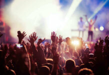 Concert crowd with hands raised, bright stage lights