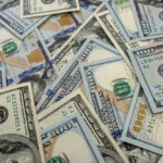 $4.9 Billion Shocker Rocks Auto Industry Scattered hundred dollar bills with Benjamin Franklins portrait.