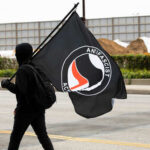 BOOM! Trump Declares Antifa Terrorists! Person dressed in black clothing holding an Antifa flag