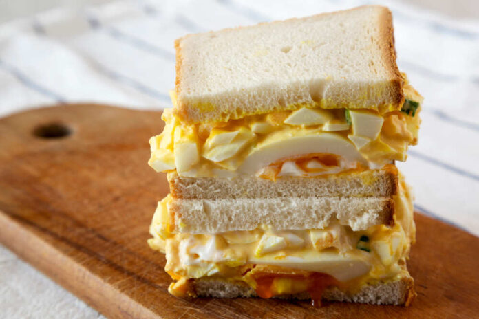 Close-up of a stacked egg sandwich on a wooden cutting board