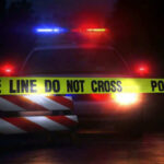 Police car with flashing lights behind caution tape