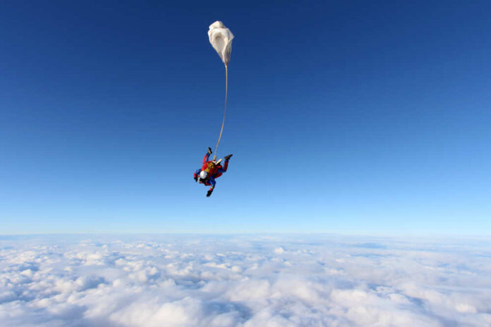 Skydiver descending through clouds with a parachute