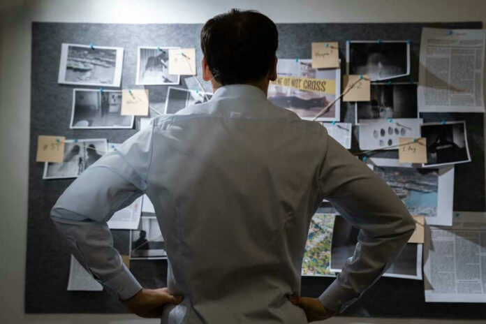 Man examining investigation board with photos and notes.