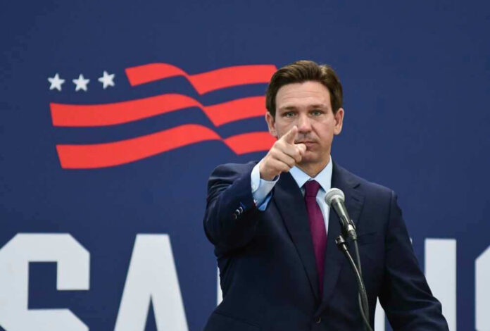 Governor of Florida, Ron DeSantis points forward at podium.