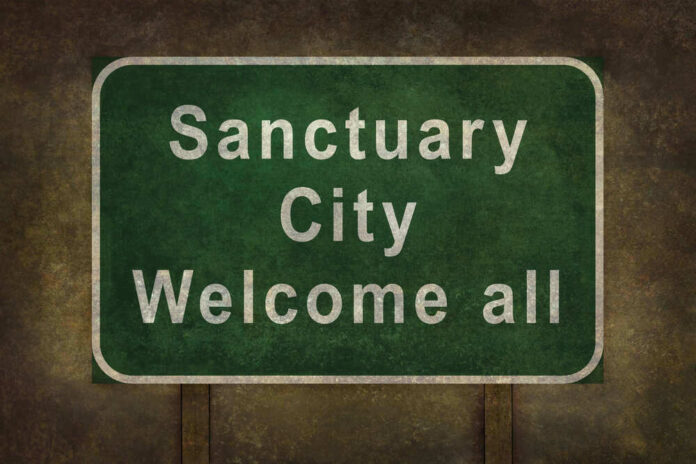 Green sign reading Sanctuary City Welcome all