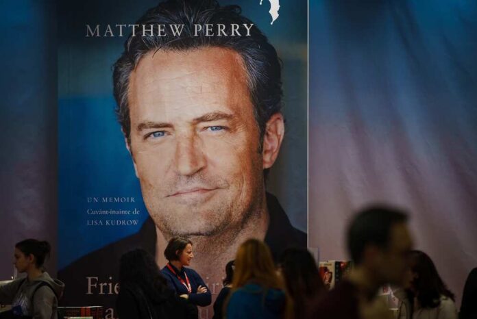 Large poster of Matthew Perry at a book signing event with fans in the foreground