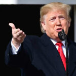 Trump SLAMS Ballroom Opposition Person speaking into a microphone, gesturing with hand.
