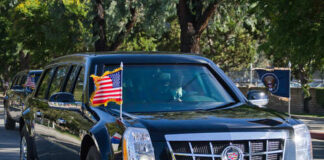 A black limousine with flags driving in a motorcade