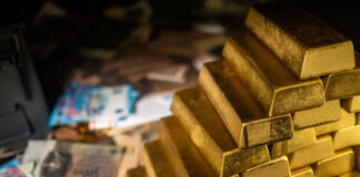 Stack of gold bars next to scattered banknotes and coins
