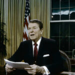 Reagan Son DIES — Conservative Movement Mourns Ronald Reagan speaking at a desk holding a paper.