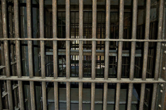 Empty, rusty barred jail cell with metal bunks.
