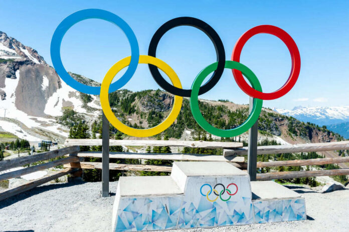 Olympic rings and podium with mountain backdrop.