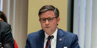Mike Johnson in a suit speaks into a microphone.