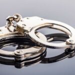 Hollywood Punk’s Mardi Gras Chaos — Arrested! Close-up of metallic handcuffs on a reflective surface