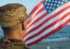 Soldier in uniform standing in front of an American flag by the ocean