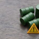 Four green barrels and a warning sign on a wooden surface