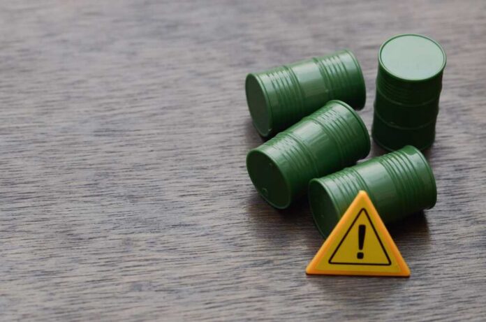 Four green barrels and a warning sign on a wooden surface