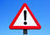 A triangular warning sign with an exclamation mark against a blue sky