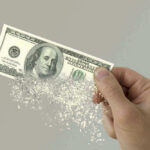 Hand holding a disintegrating hundred dollar bill.