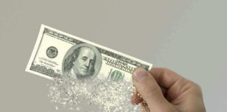 Hand holding a disintegrating hundred dollar bill.