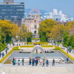 Visitors at Hiroshima Peace Memorial Park with cherry blossoms and memorial structures