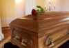 A wooden casket with a red rose placed on top