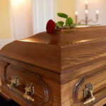 A wooden casket with a red rose placed on top