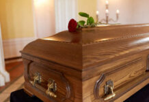 A wooden casket with a red rose placed on top