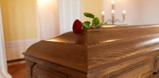 A wooden casket with a red rose placed on top