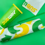 SUBWAY UNLEASHES $5 Protein Menu Subway sandwich wrapped in branded paper next to a green beverage cup