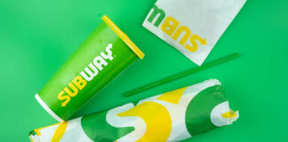 Subway sandwich wrapped in branded paper next to a green beverage cup
