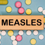 Measles Explosion Finally Ended Wooden block with the word 'MEASLES' surrounded by various pills