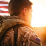 Delta Force Deployed After Baghdad Kidnapping Nightmare Soldier in camouflage facing American flag at sunset.