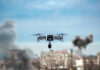 Drone flying over urban area with smoke plumes.