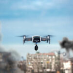 Drone flying over urban area with smoke plumes.