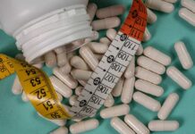 White capsules scattered around a measuring tape and a bottle