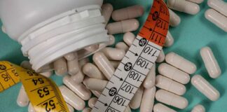 White capsules scattered around a measuring tape and a bottle